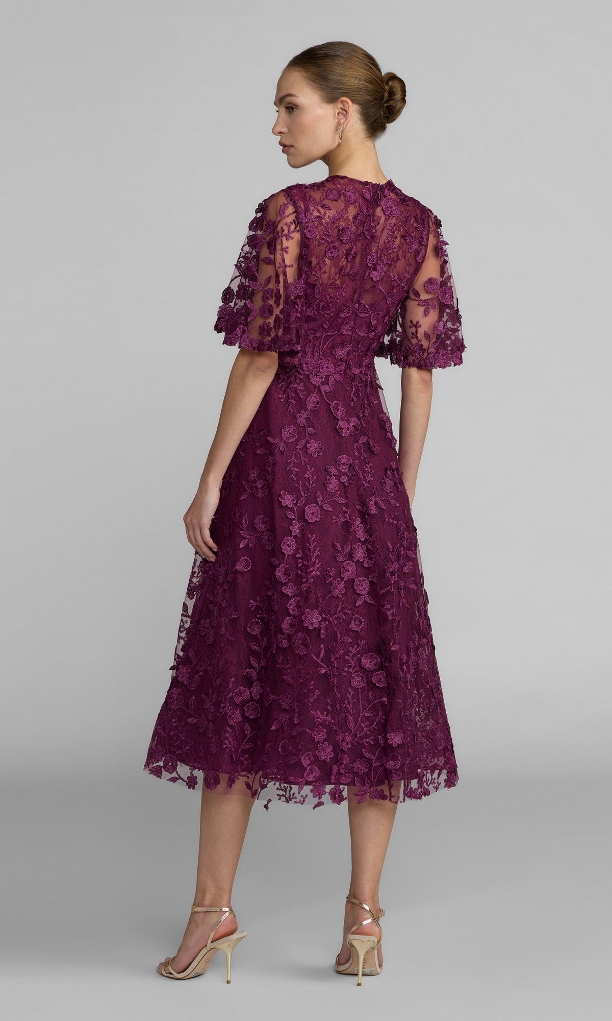 Woman in profile wears the Mac Duggal 69036 Lace Midi Wedding Guest Dress—short sleeves, purple floral lace—set against a plain backdrop. Ideal for wedding guests.